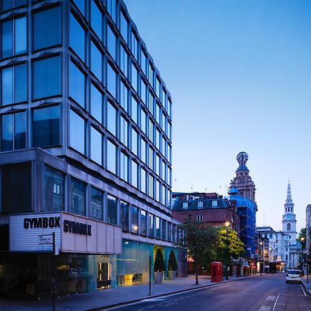 Hotel St Martins Lane Londýn Exteriér fotografie The photo shows a street scene during twilight, featuring a modern, glass-fronted building on the left side, which appears to be a gym called "GYMBOK GYM." On the right, there are more traditional architectural elements, including a tower and a steep
