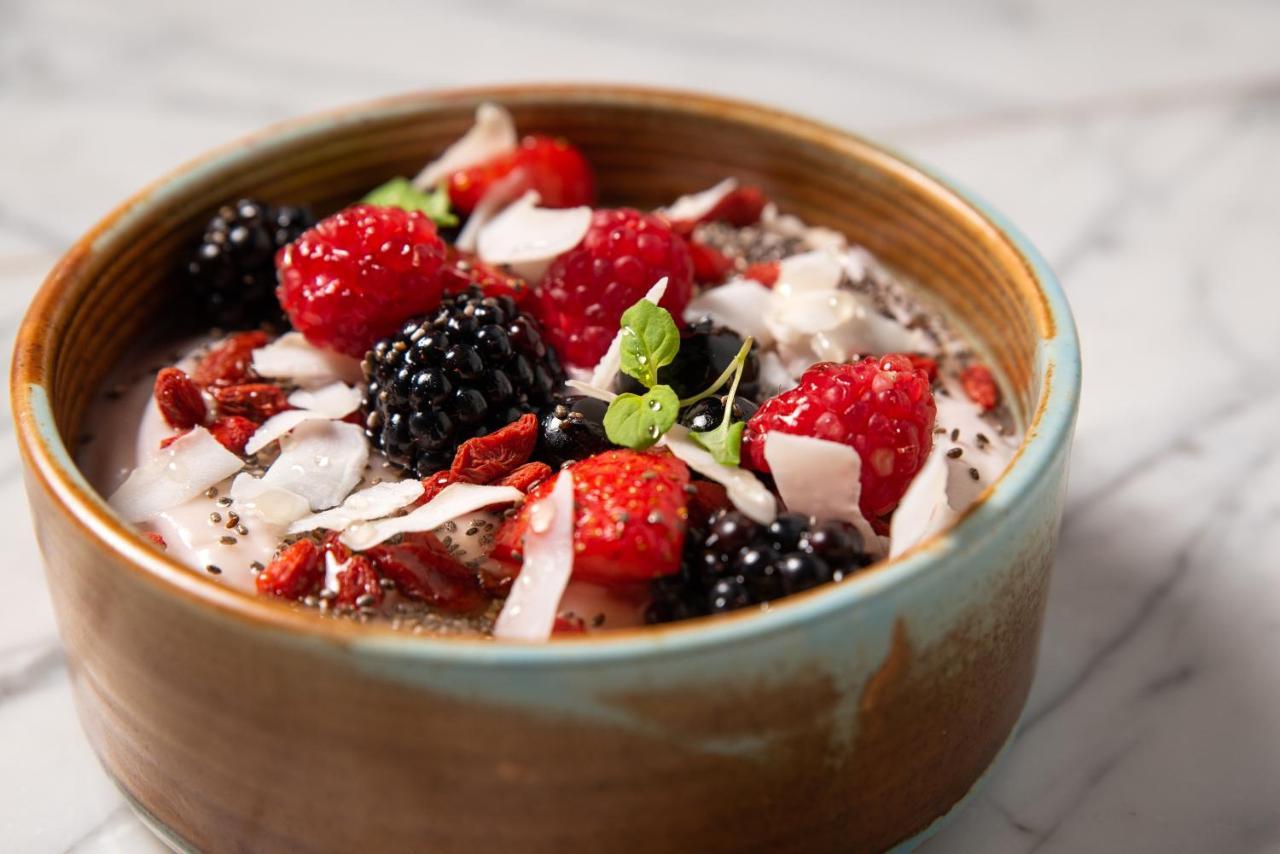 Hotel St Martins Lane Londýn Exteriér fotografie The photo shows a bowl of yogurt topped with various fresh fruits and toppings. The toppings include vibrant red raspberries, blackberries, and pieces of dried fruits, along with shredded coconut. There are also some small seeds, possibly chia seeds,