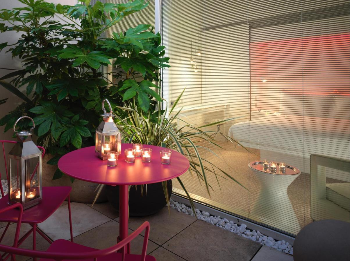 Hotel St Martins Lane Londýn Exteriér fotografie The photo depicts a cozy outdoor space with a round pink table and two matching chairs. On the table, there are several lanterns with candles inside, providing a warm ambiance. Surrounding the area are lush green plants, adding a natural touch. In th