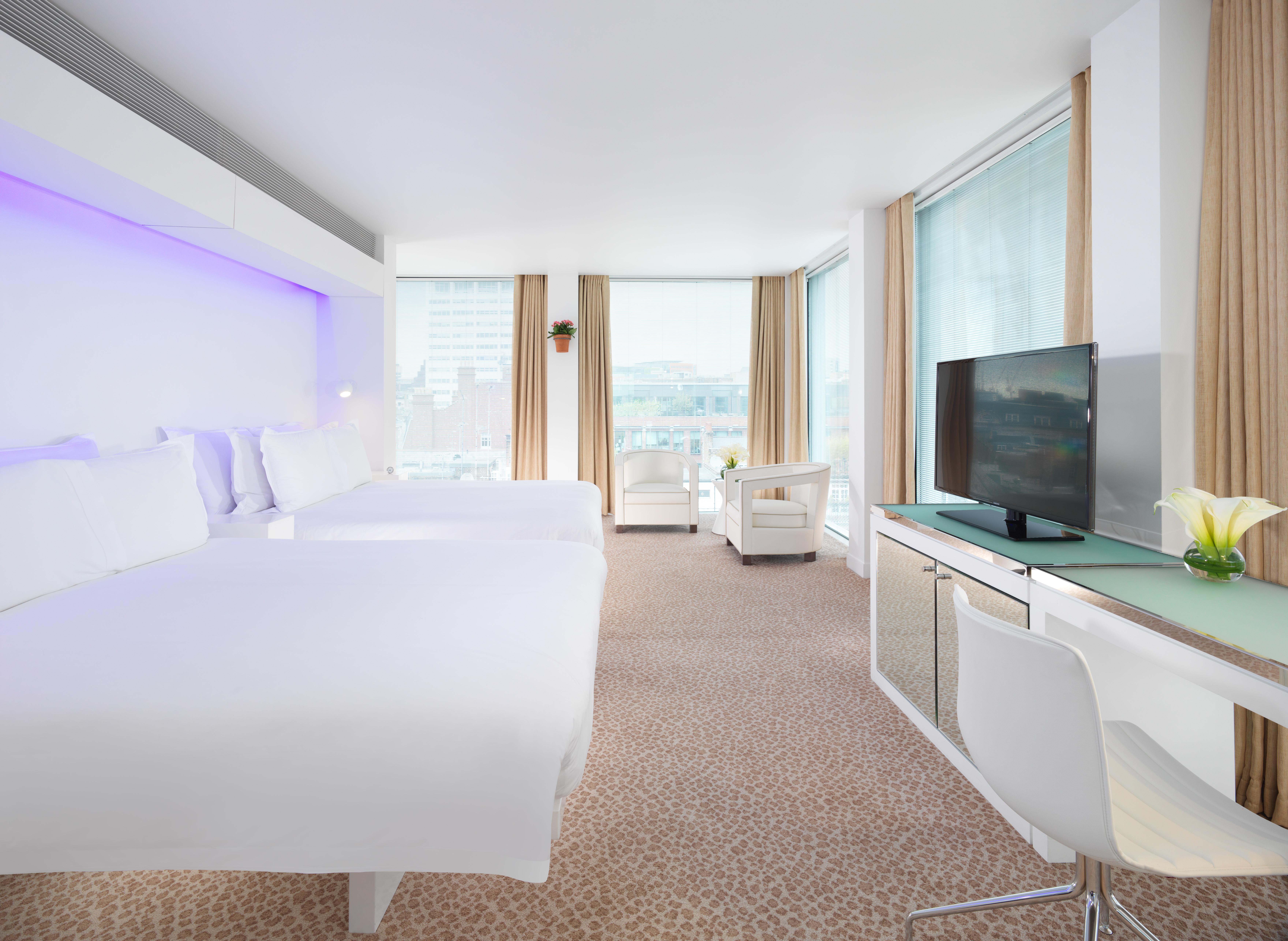 Hotel St Martins Lane Londýn Exteriér fotografie The photo shows a modern hotel room featuring two beds with white linens, a sleek design, and large windows allowing natural light to enter. The room includes a comfortable chair, a desk with a television mounted on the wall, and a stylish decorative