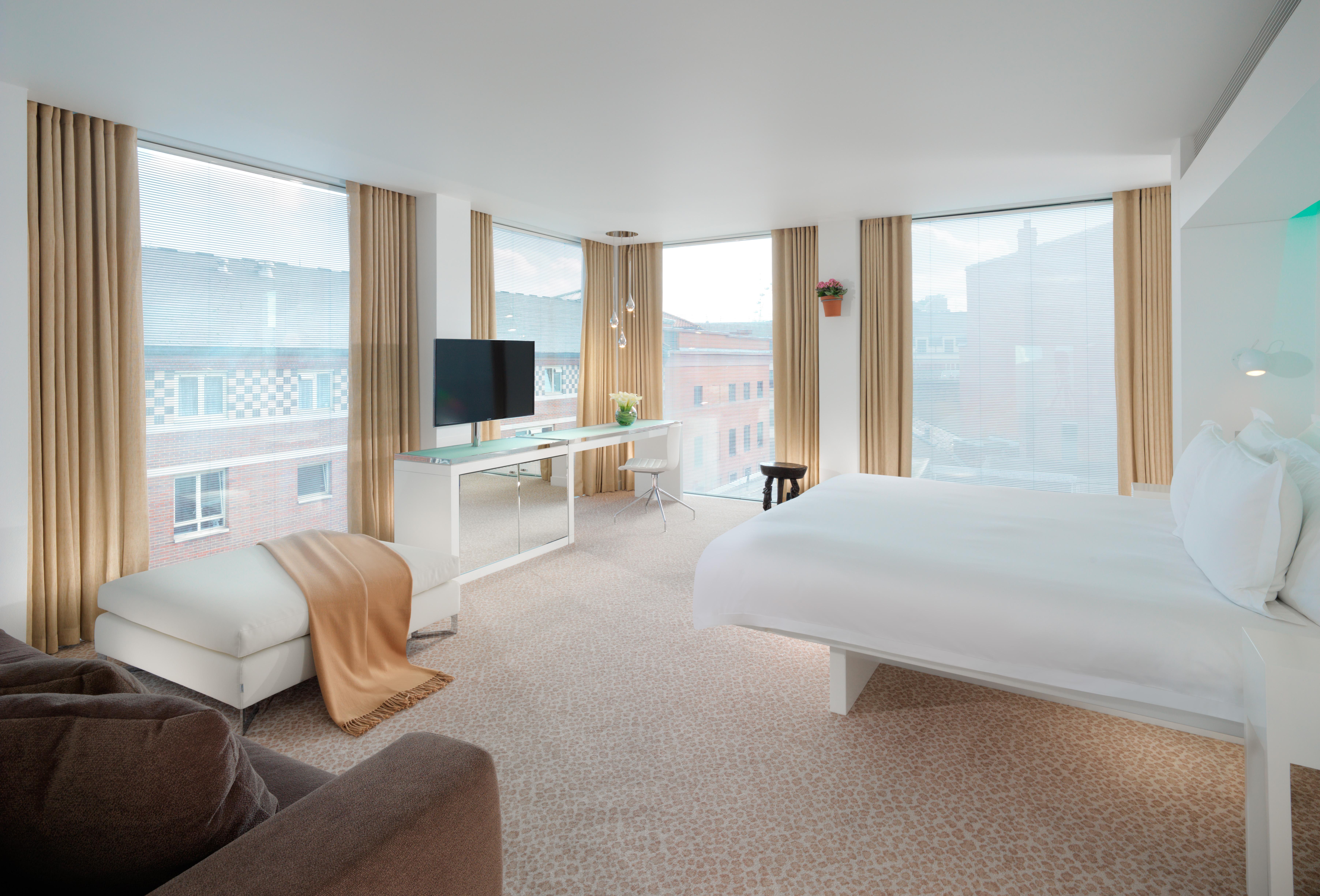 Hotel St Martins Lane Londýn Exteriér fotografie The photo displays a modern hotel room that features large windows allowing natural light to fill the space. The room includes a comfortable bed with white linens, a cozy chair and a throw blanket in neutral tones, and a small side table. There is a 