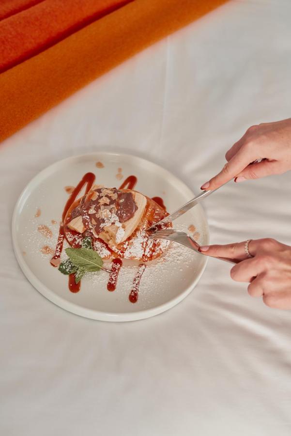 Hotel St Martins Lane Londýn Exteriér fotografie The photo depicts a dessert served on a white plate. A person is using a fork and knife to cut into a piece of the dessert, which appears to be a layered cake or pastry topped with chocolate and perhaps caramel sauce. The dessert is garnished with po