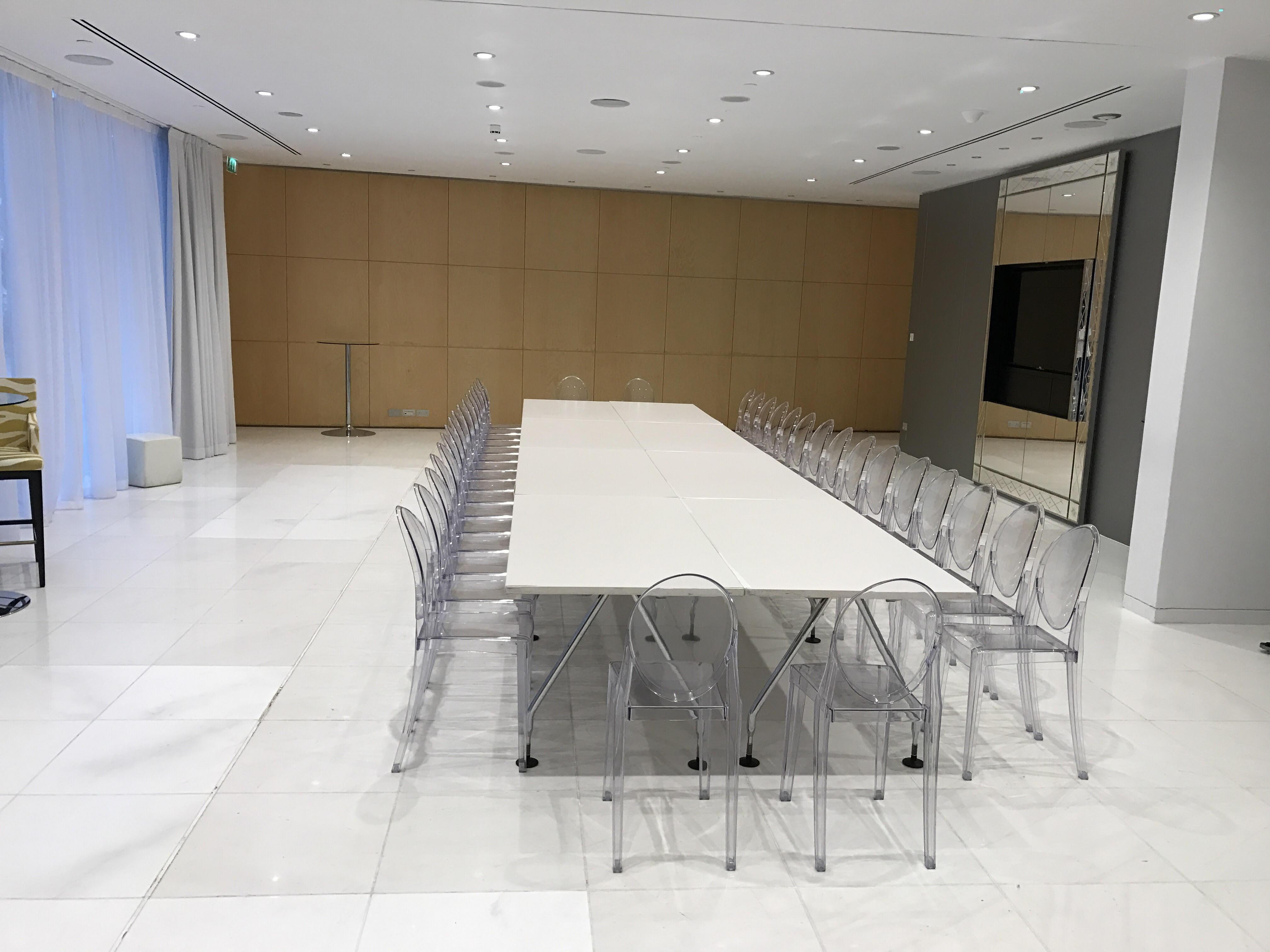 Hotel St Martins Lane Londýn Exteriér fotografie The photo shows a modern meeting room or conference space. There is a long rectangular table in the center, surrounded by transparent acrylic chairs. The room features white marble flooring and appears bright due to the overhead lighting. On one side