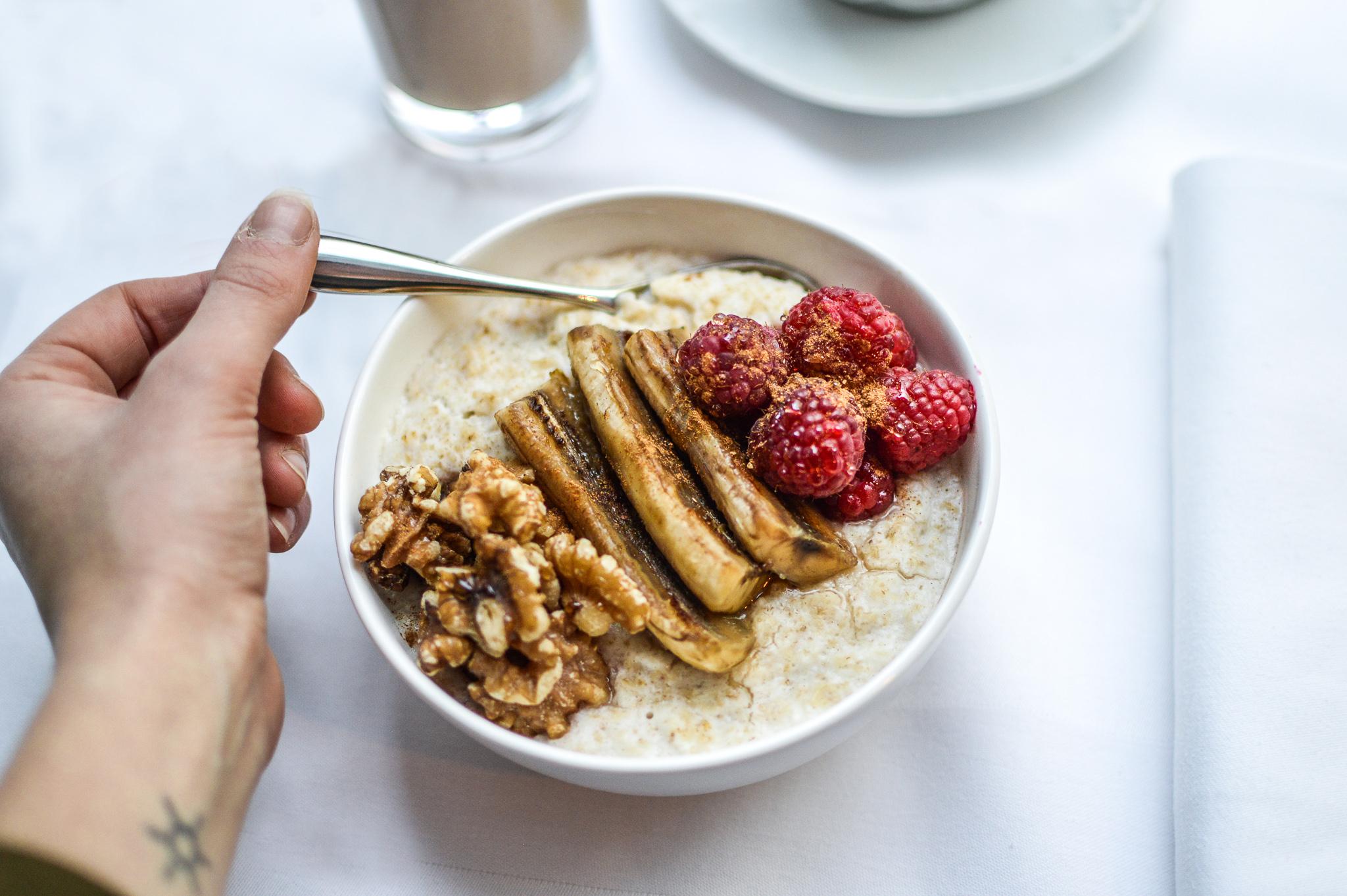 Hotel St Martins Lane Londýn Exteriér fotografie The photo shows a bowl of oatmeal topped with sliced bananas, raspberries, and walnuts. A hand holding a spoon is reaching towards the bowl. In the background, there's a glass of a beverage and a plate, suggesting a breakfast setting. The overall pre