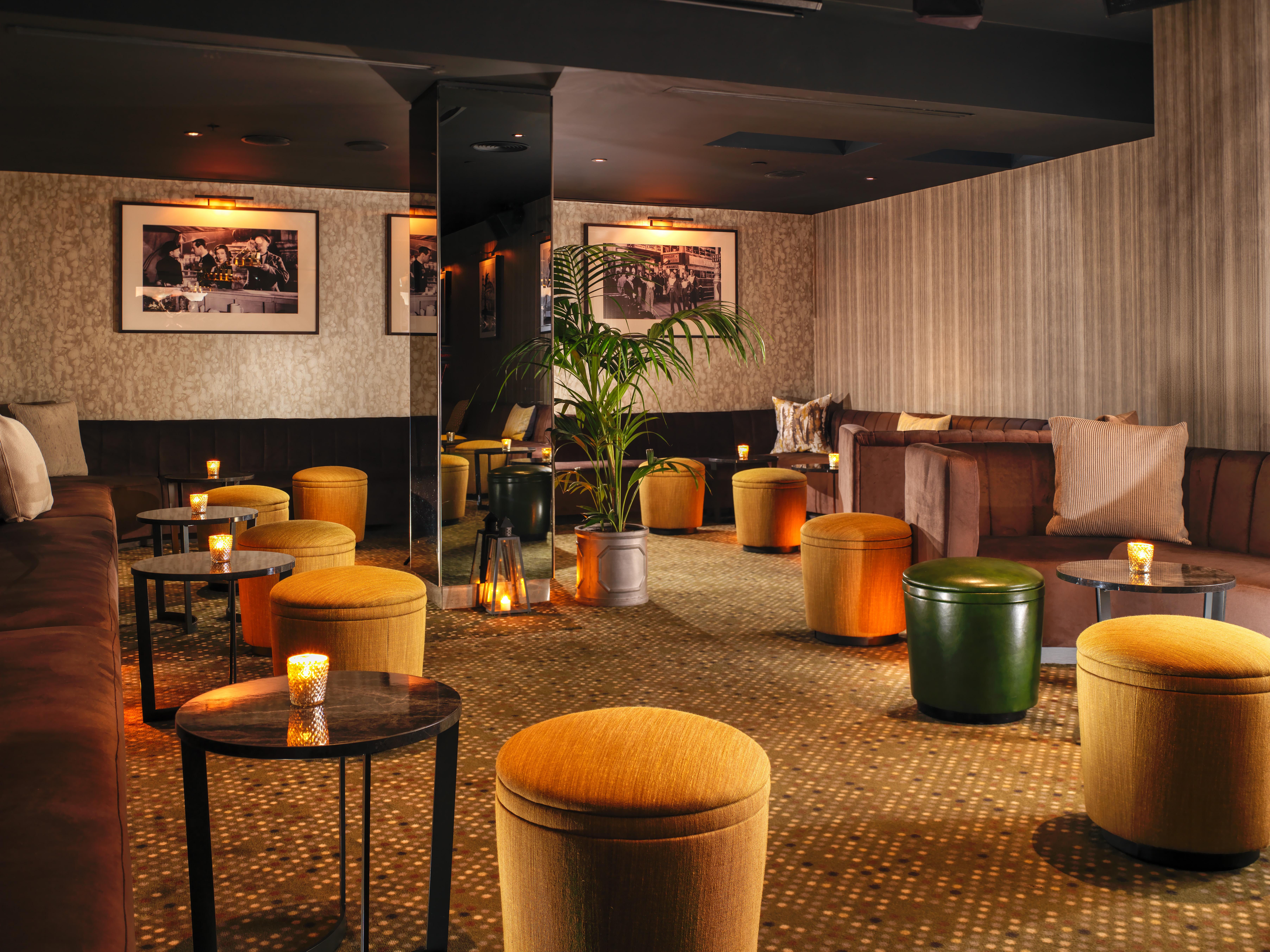 Hotel St Martins Lane Londýn Exteriér fotografie The photo shows a cozy lounge area with a warm and inviting atmosphere. The space features a mix of seating arrangements, including cushioned benches and small round tables. There are several colorful ottomans, predominantly in shades of yellow and g