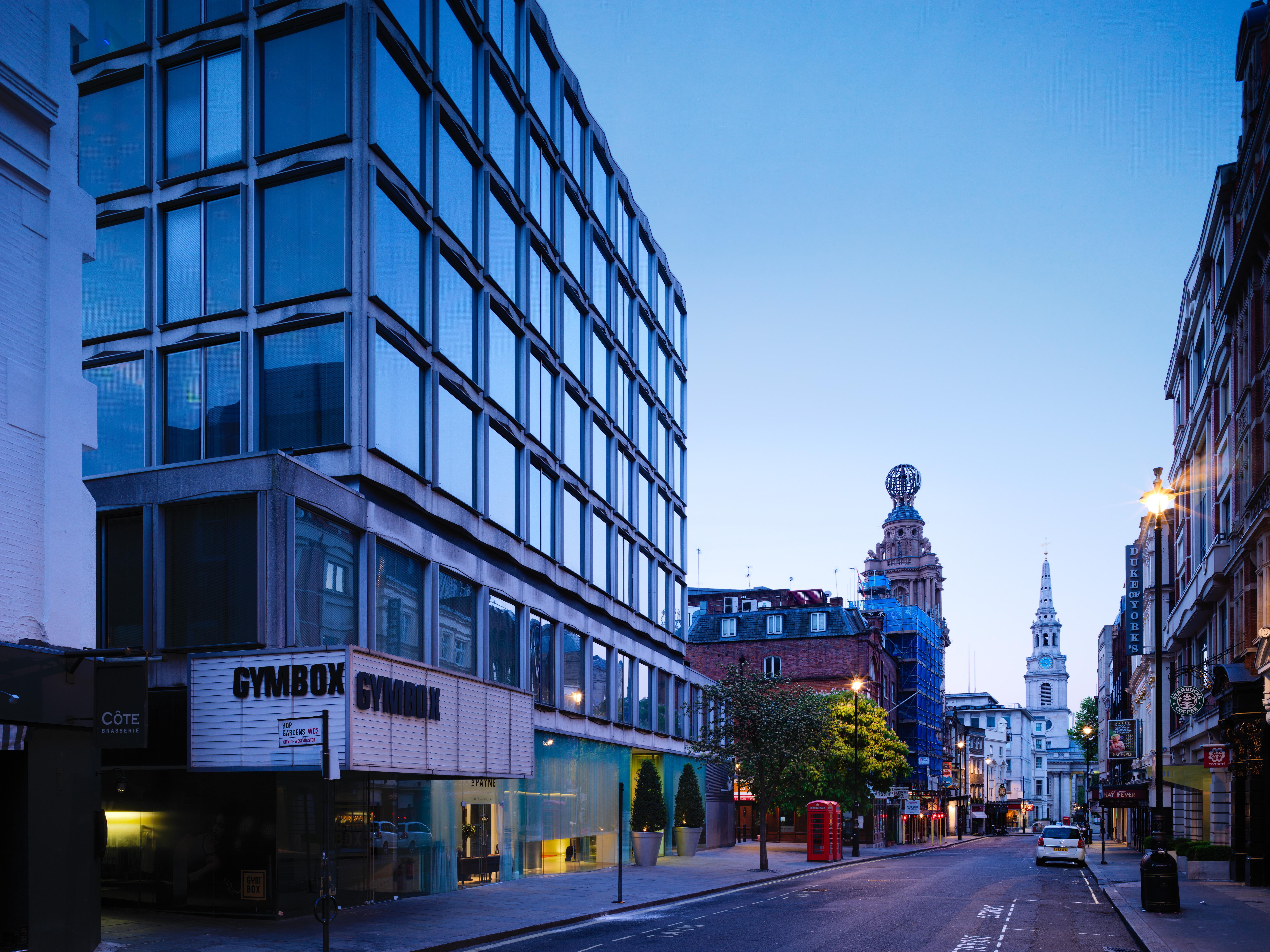 Hotel St Martins Lane Londýn Exteriér fotografie The photo shows a street scene during twilight, featuring a modern, glass-fronted building on the left side, which appears to be a gym called "GYMBOK GYM." On the right, there are more traditional architectural elements, including a tower and a steep