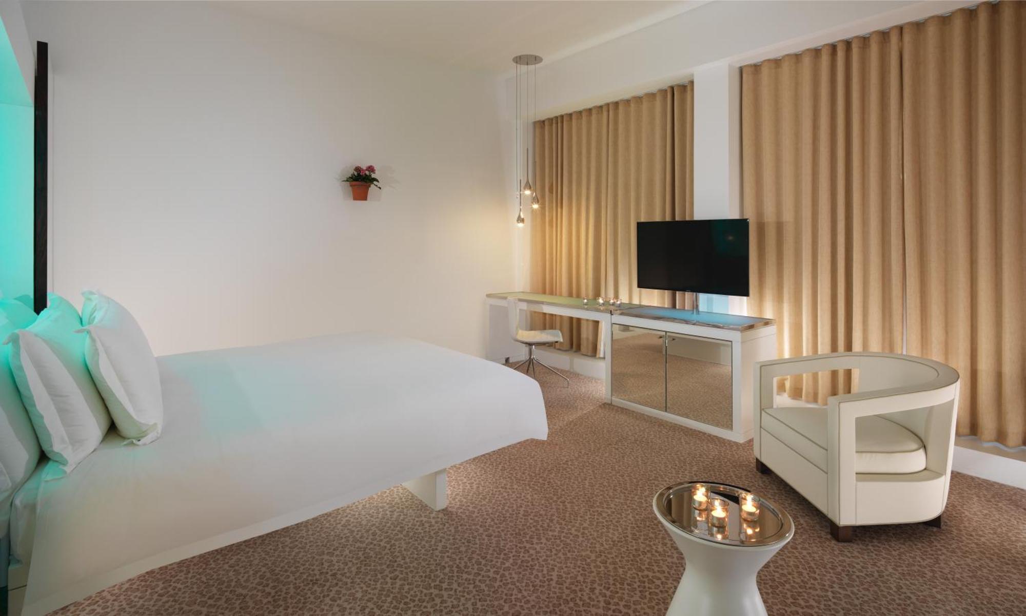 Hotel St Martins Lane Londýn Exteriér fotografie The photo shows a modern hotel room with a minimalist design. It features a large bed against one wall, a flat-screen TV mounted on another wall, and a contemporary desk with a mirror. Large windows are dressed with light-colored curtains, allowing n