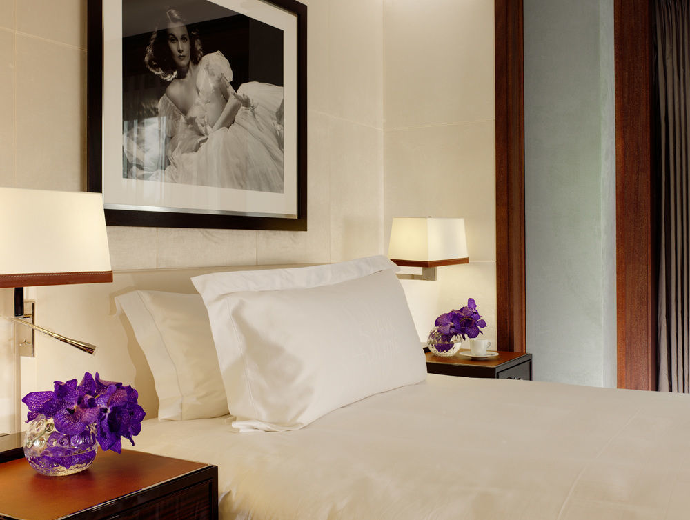 Hotel St Martins Lane Londýn Exteriér fotografie The photo shows a stylishly decorated bedroom. It features a neatly made bed with a white bedspread and a large white pillow. On either side of the bed, there are dark wood nightstands with decorative lamps. Each nightstand has a small vase containin