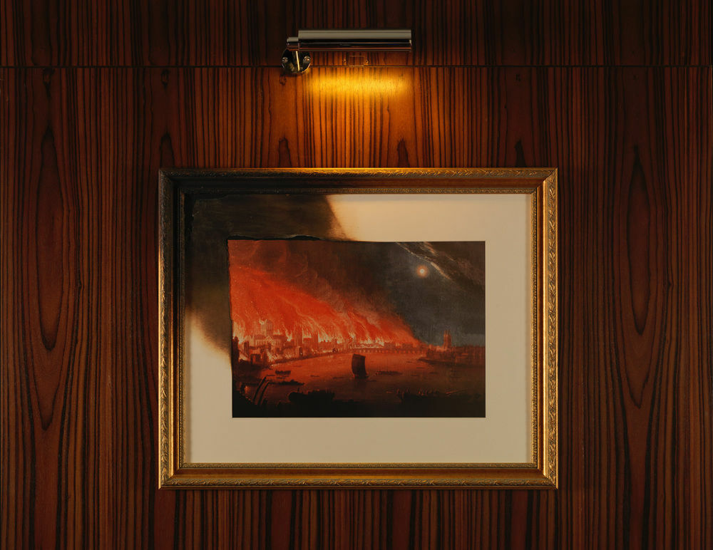Hotel St Martins Lane Londýn Exteriér fotografie The photo shows a framed painting illuminated by a small light above it. The artwork depicts a dramatic scene with fiery red and orange hues, suggesting a sense of destruction or chaos. The painting is set against a wall with a wood grain texture, an