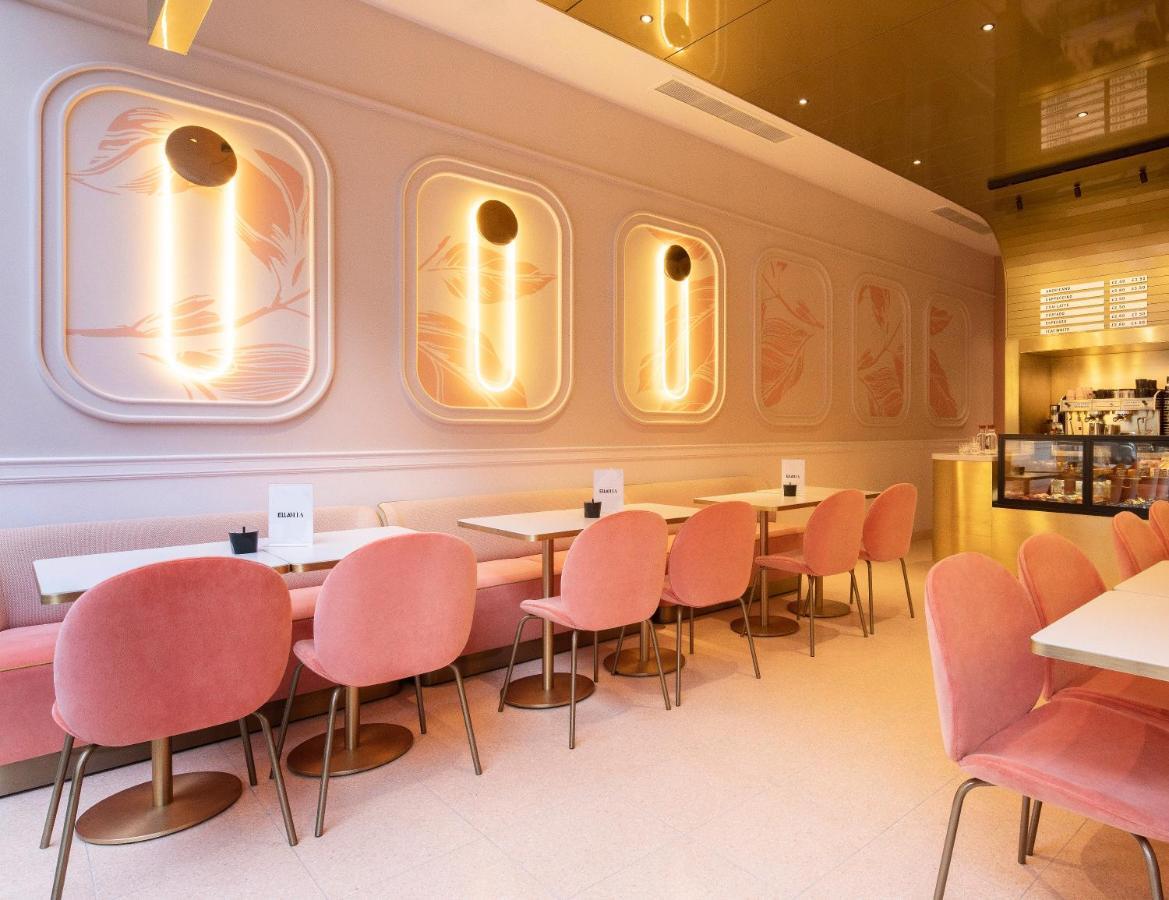 Hotel St Martins Lane Londýn Exteriér fotografie The photo depicts a stylish cafe or restaurant interior. The walls are adorned with soft pastel colors, particularly muted pink tones, and feature elegant, abstract designs. There are modern pendant lights mounted on the walls, which provide warm lig